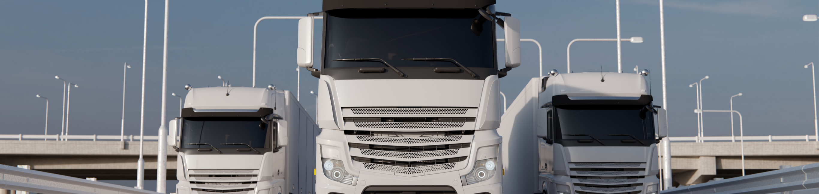 Vista frontal de una flota de camiones de gran tonelaje alineados en autopista, con diseño aerodinámico y ópticas LED, representando logística moderna y transporte profesional.